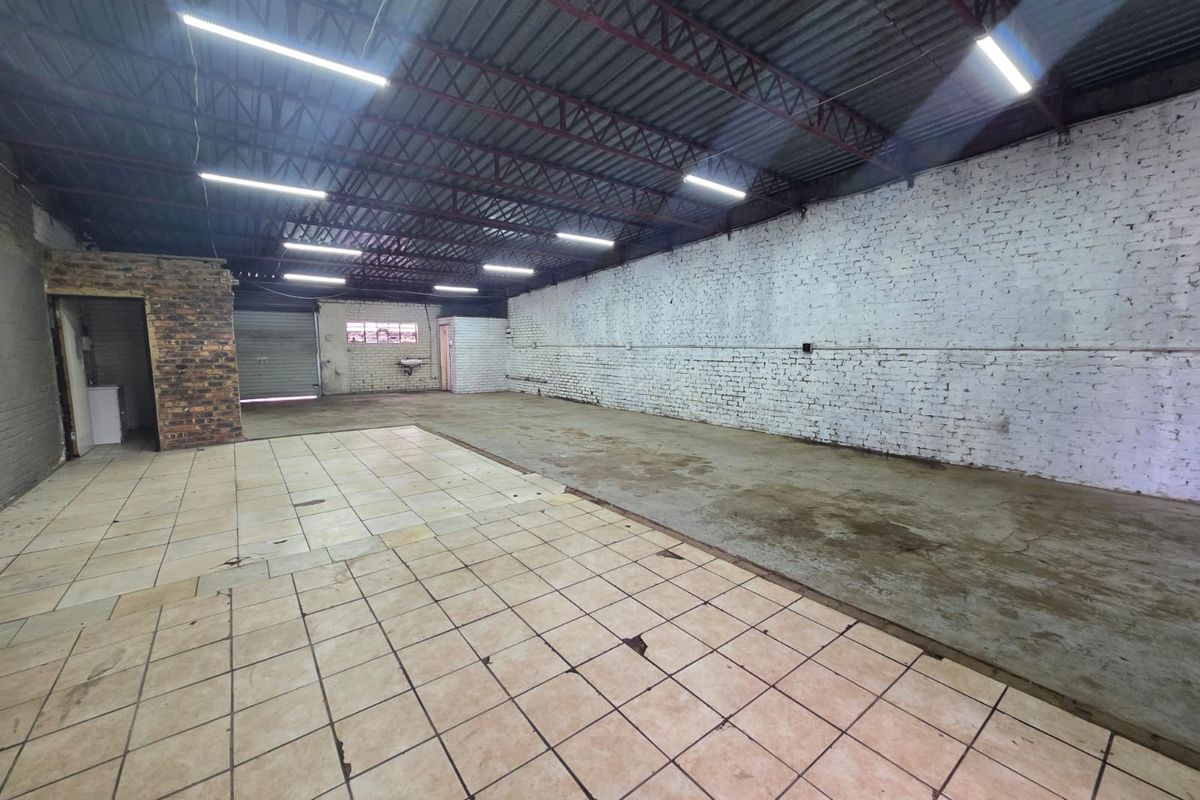Spacious industrial warehouse or commercial space featuring exposed brick walls, tiled and concrete flooring, and high-clearance ceilings with integrated lighting.
