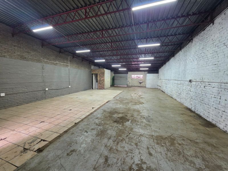 Spacious open-plan industrial or commercial unit featuring high exposed ceilings, concrete and tiled flooring, and ample lighting, suitable for various business operations.
