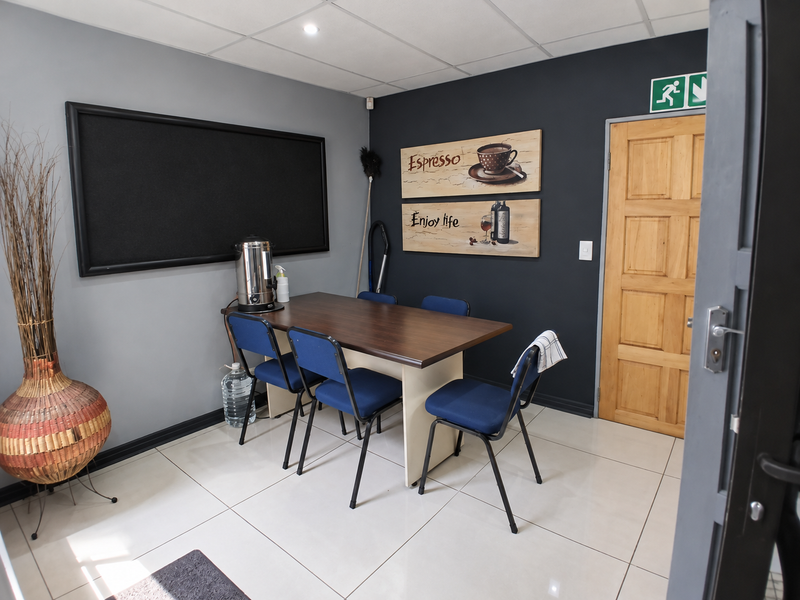 A functional office space featuring tiled flooring, a suspended ceiling, and a solid wooden door with an emergency exit sign.