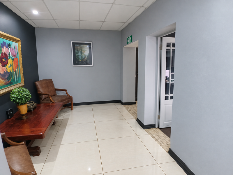 A well-maintained office hallway featuring large format floor tiles, a suspended ceiling with recessed lighting, and a classic panelled door.