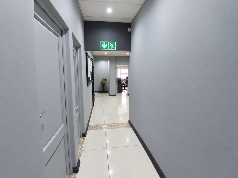 A clean, well-lit commercial hallway featuring neutral grey walls, polished tiled flooring, and a drop ceiling with recessed lighting.