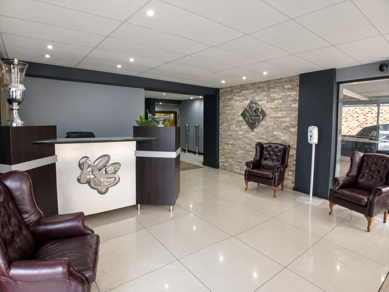 Professional business reception area featuring a modern reception desk, stone feature wall, polished tiled flooring, and recessed ceiling lighting.