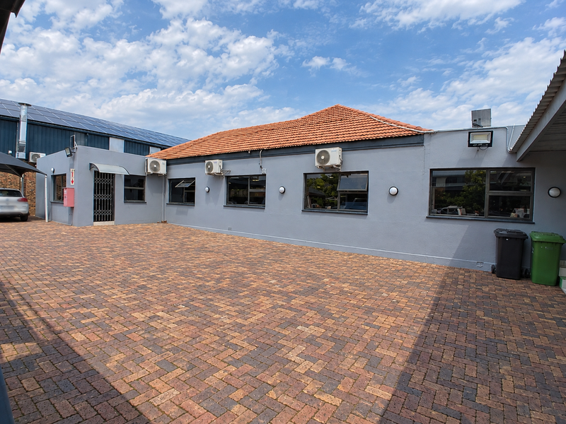 A well-maintained paved rear courtyard area featuring grey exterior walls, terracotta roof tiles, and multiple wall-mounted air conditioning units.