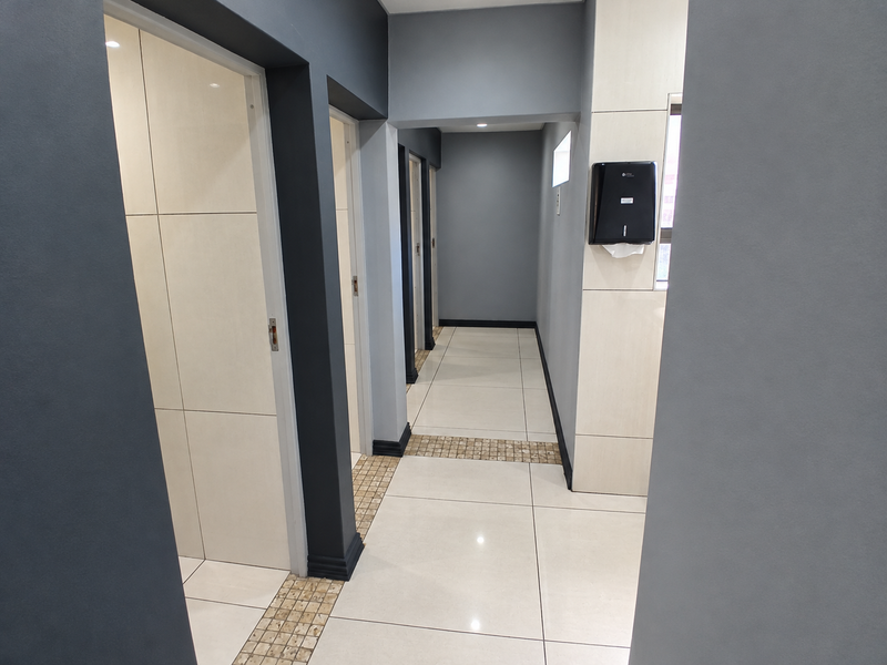 A clean, modern commercial hallway featuring large format floor tiles, contrasting grey and cream wall finishes, and recessed ceiling lighting.