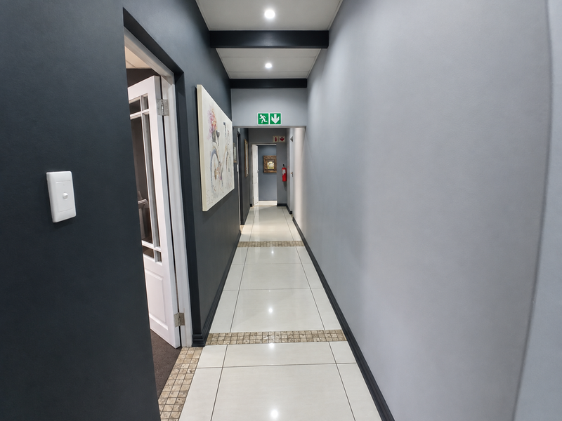A clean, well-lit commercial hallway featuring modern grey walls, tiled flooring with decorative accents, and essential safety signage.