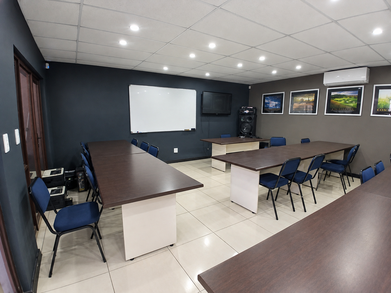 A functional office or meeting room featuring tiled flooring, a suspended ceiling with recessed lighting, and a wall-mounted air conditioning unit.