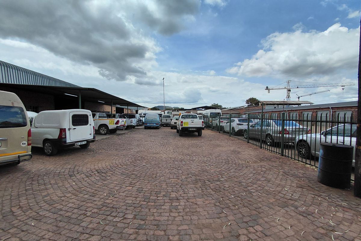 A paved outdoor parking area featuring a covered industrial structure and perimeter metal fencing.