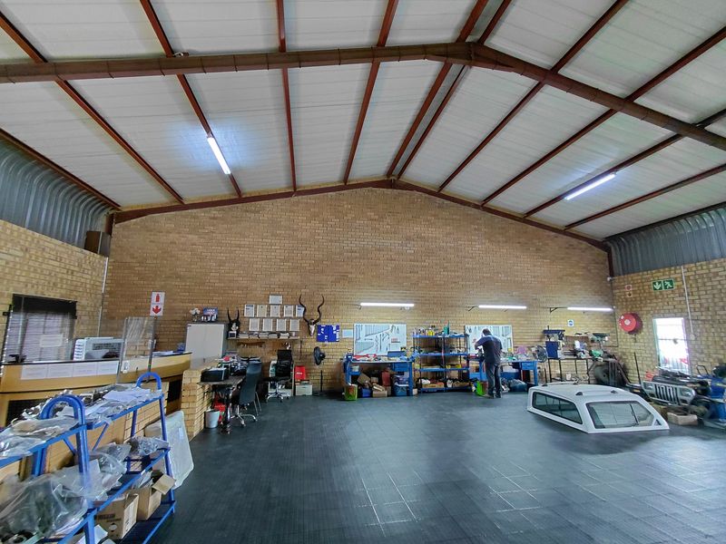 Spacious industrial workshop area featuring high vaulted ceilings, exposed brick walls, and durable flooring, suitable for various commercial or automotive business operations.