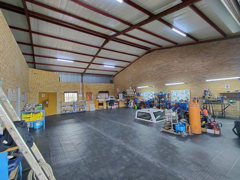 Spacious industrial workshop featuring high-pitched steel truss roofing, exposed brick walls, and durable rubberized flooring, suitable for various commercial or trade operations.