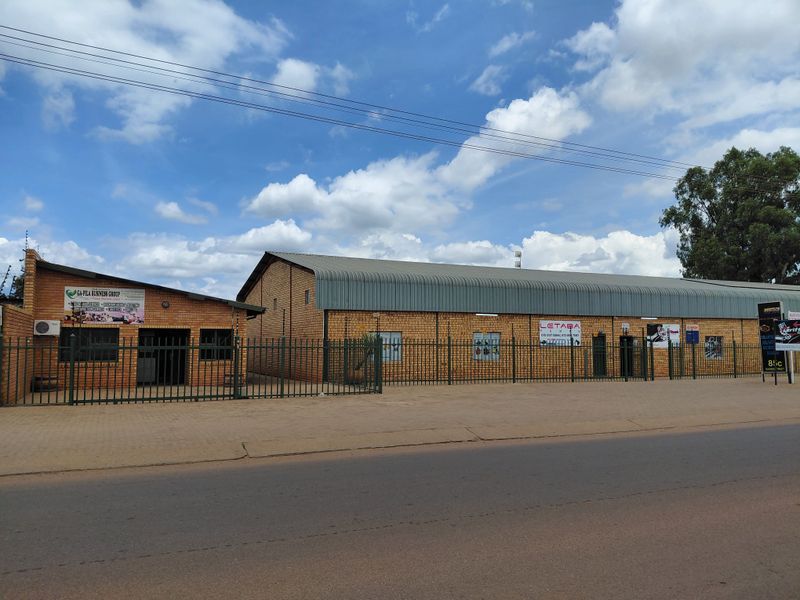 Street-facing view of a commercial property featuring brick warehouse buildings, secure perimeter fencing, and multiple business signage displays.