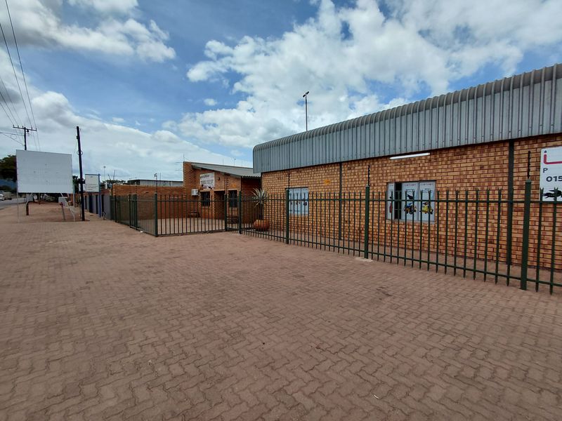 Exterior view of a commercial brick building featuring paved frontage, secure perimeter fencing, and metal roofing.