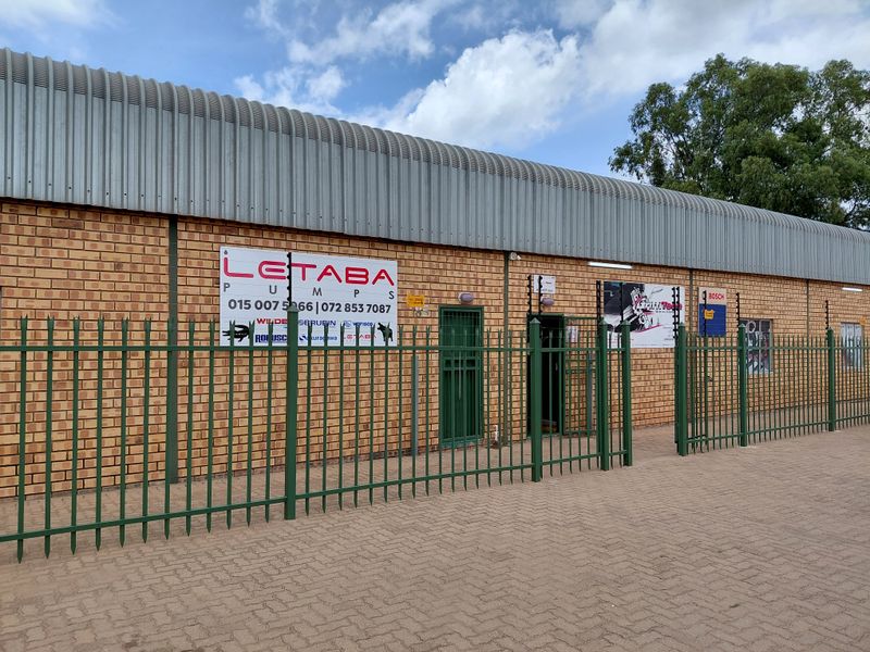 Front exterior view of a commercial building featuring face brick walls, corrugated metal roofing, and secure perimeter fencing with gated access.