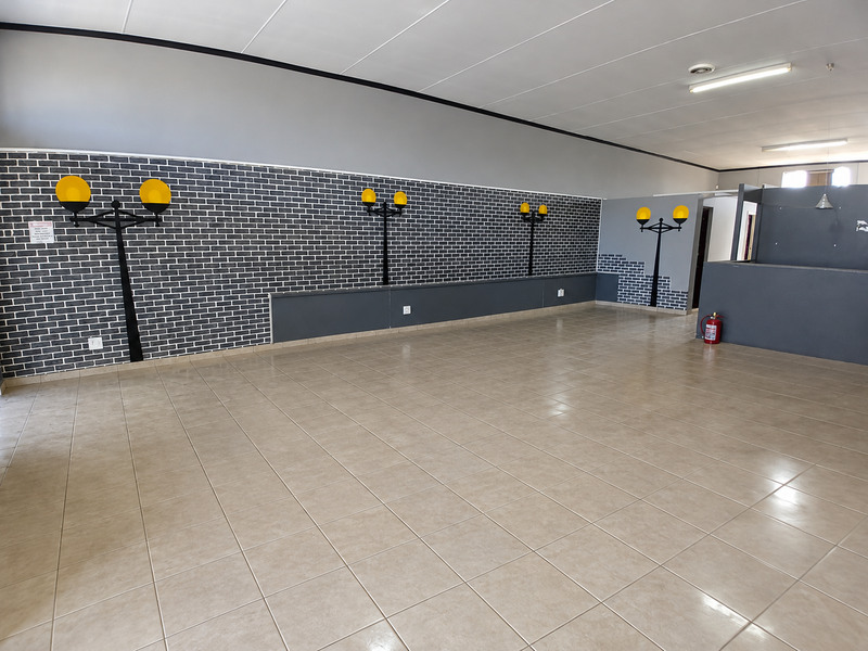 A spacious, empty commercial open-plan area featuring tiled flooring, a suspended ceiling, and decorative wall-mounted lighting fixtures.