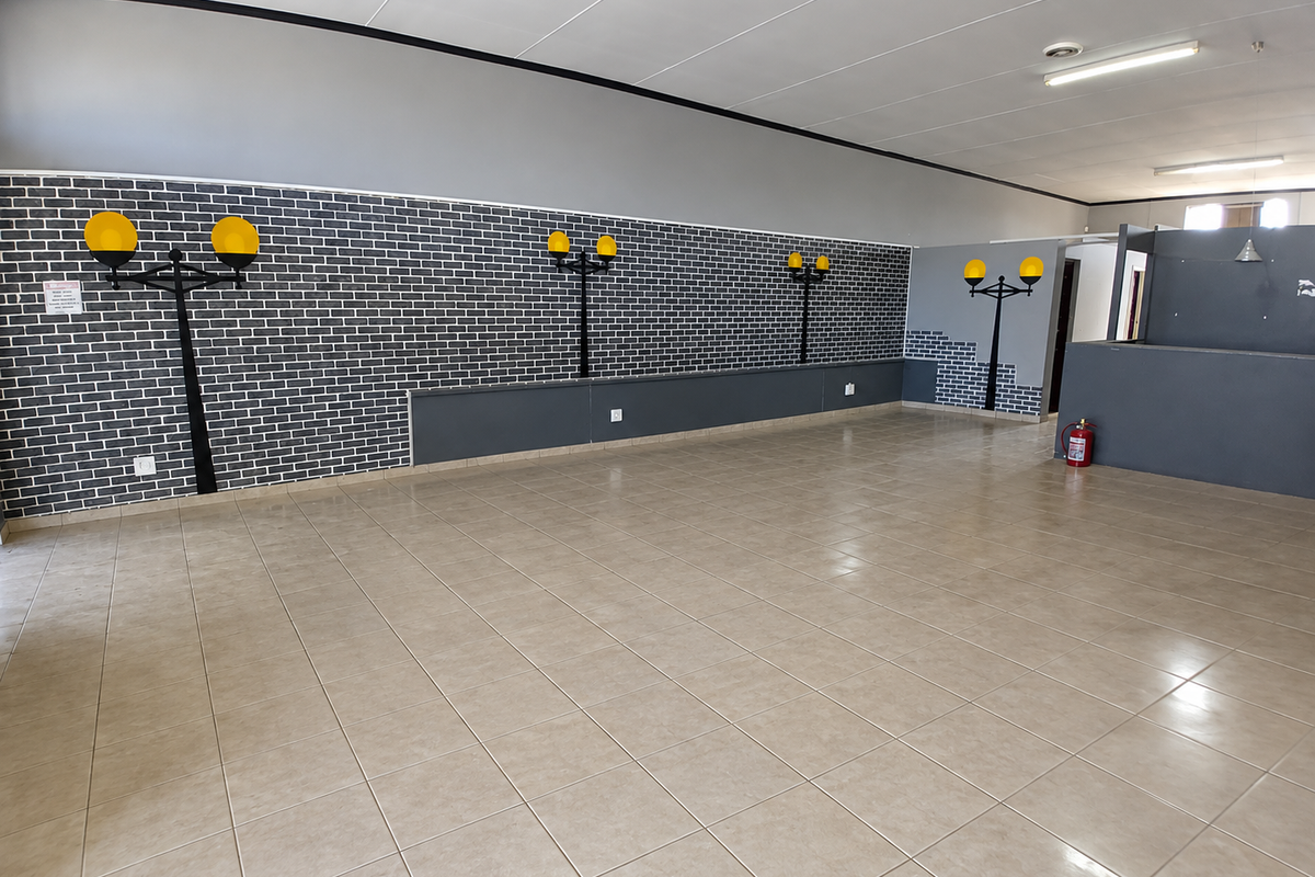 A spacious, empty commercial open-plan area featuring tiled flooring, a suspended ceiling, and decorative wall-mounted lighting fixtures.