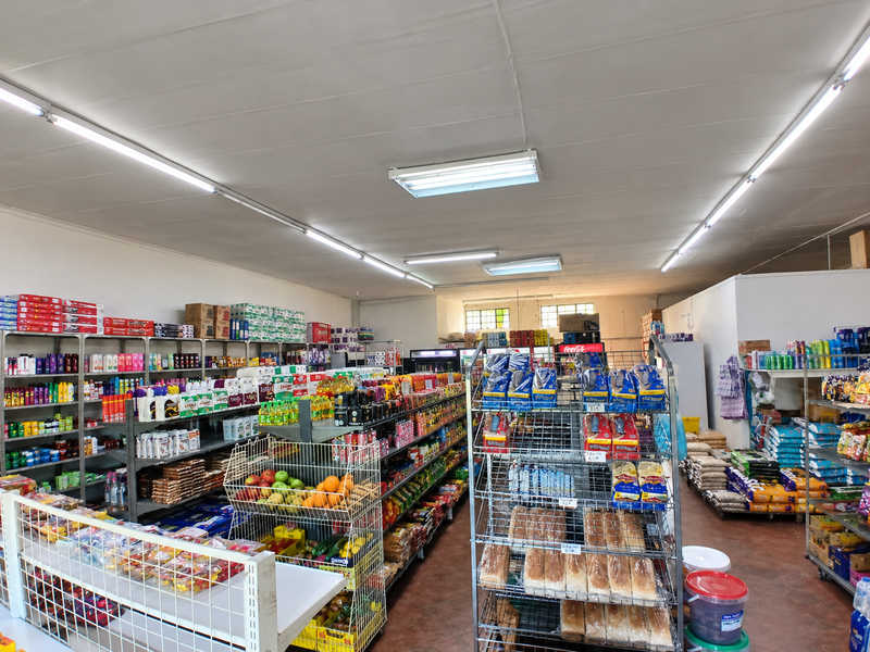 A commercial retail space featuring extensive metal shelving units, fluorescent overhead lighting, and durable tiled flooring throughout the open-plan layout.