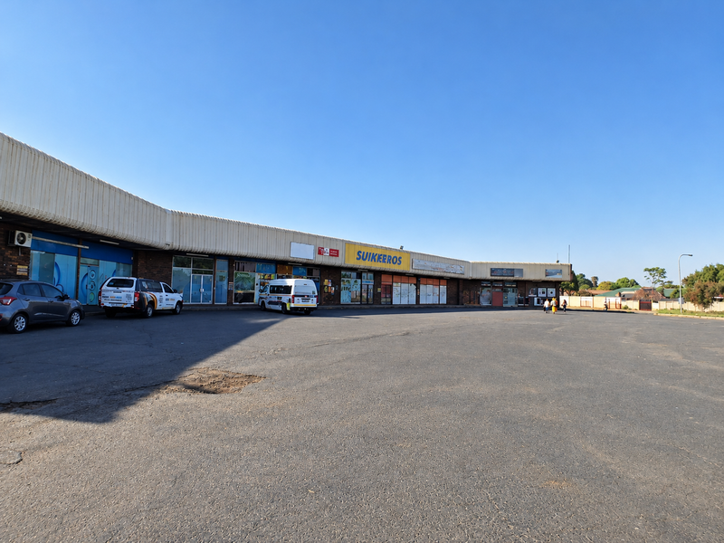 A commercial strip mall featuring multiple storefronts with signage and an expansive asphalt parking area in front.