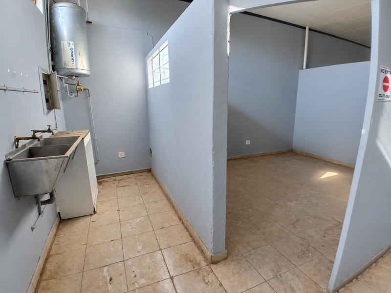 A functional utility space featuring a stainless steel sink, electric water heater, and tiled flooring, suitable for commercial storage or service requirements.