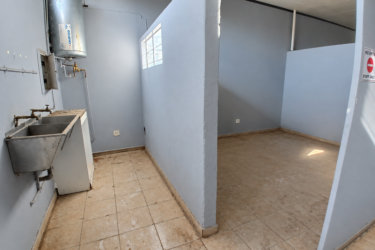 A functional utility space featuring a stainless steel sink, electric water heater, and tiled flooring, suitable for commercial storage or service requirements.