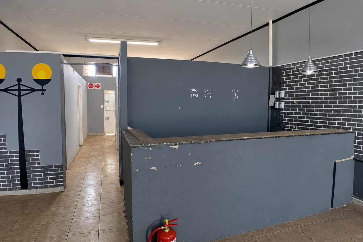 Commercial office space featuring a built-in reception counter, tiled flooring, and modern pendant lighting, suitable for a professional reception or service area.