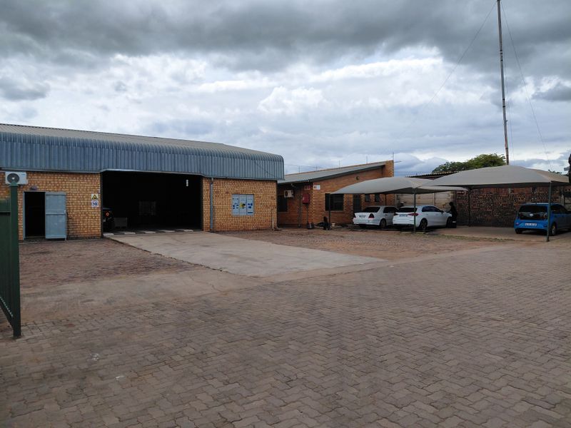 Industrial property featuring a large warehouse unit, paved yard area, and covered parking bays for multiple vehicles.