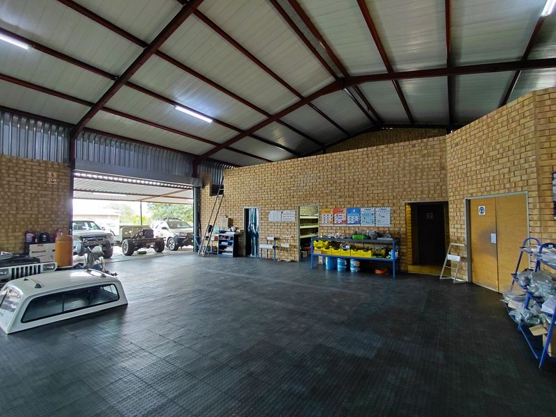 Spacious industrial workshop or garage area featuring exposed brick walls, high-pitched steel roof structure, and durable rubberized flooring.