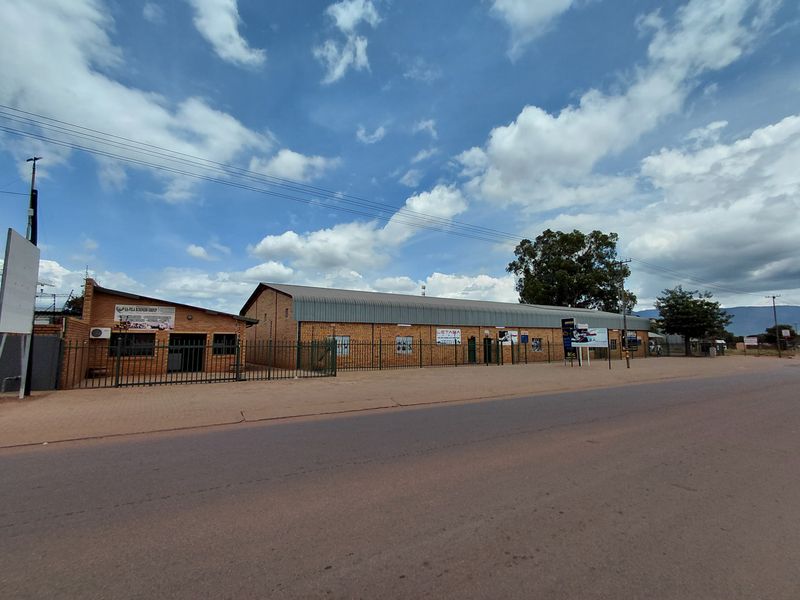 Street-facing view of a commercial property complex featuring brick construction, metal roofing, and perimeter security fencing.