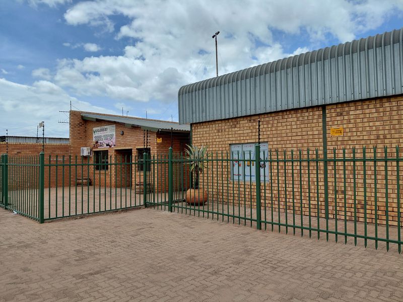 Exterior view of a commercial property featuring face-brick construction, secure perimeter fencing, and paved driveway area.
