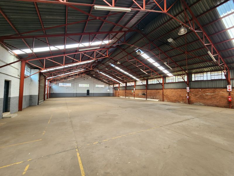 Spacious industrial warehouse featuring high exposed steel trusses, concrete flooring, natural light from skylights, and functional brick wall construction.