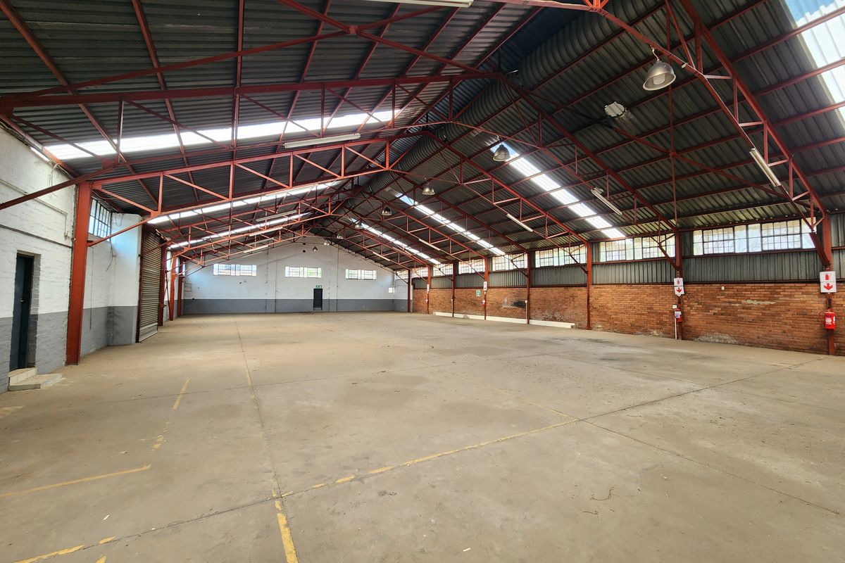 Spacious industrial warehouse featuring high exposed steel trusses, concrete flooring, natural light from skylights, and functional brick wall construction.