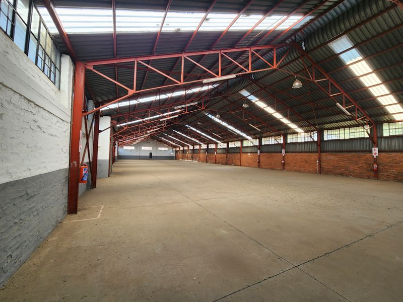 Spacious industrial warehouse featuring exposed steel roof trusses, concrete flooring, brick walls, and natural light through integrated skylights.
