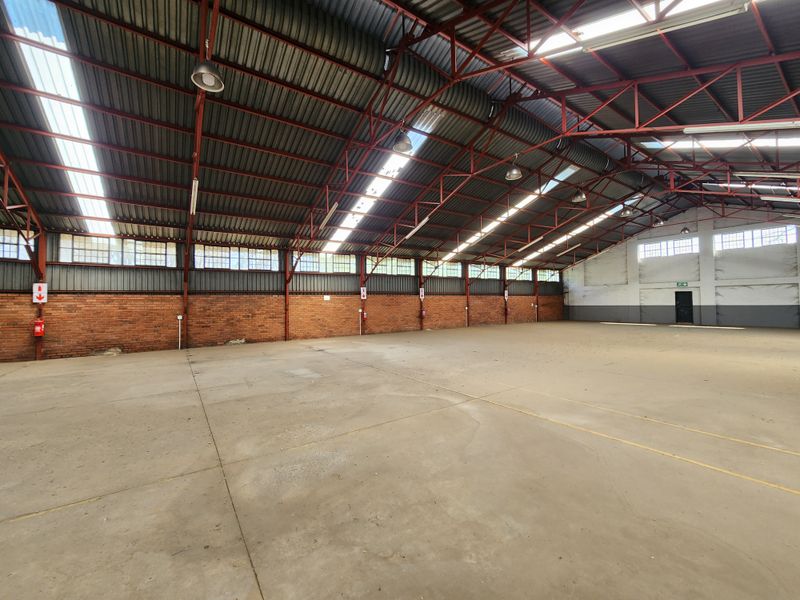 Spacious industrial warehouse featuring high exposed steel truss ceilings, concrete flooring, natural light from skylights, and durable brick wall construction.