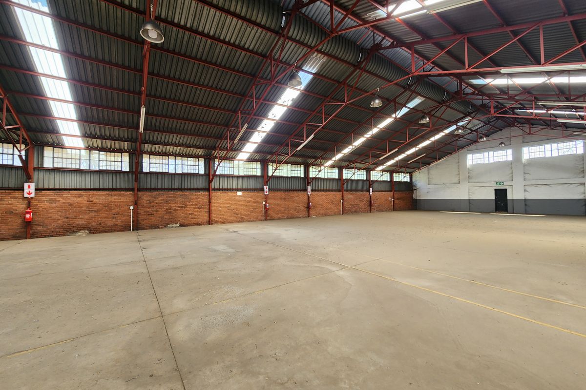 Spacious industrial warehouse featuring high exposed steel truss ceilings, concrete flooring, natural light from skylights, and durable brick wall construction.