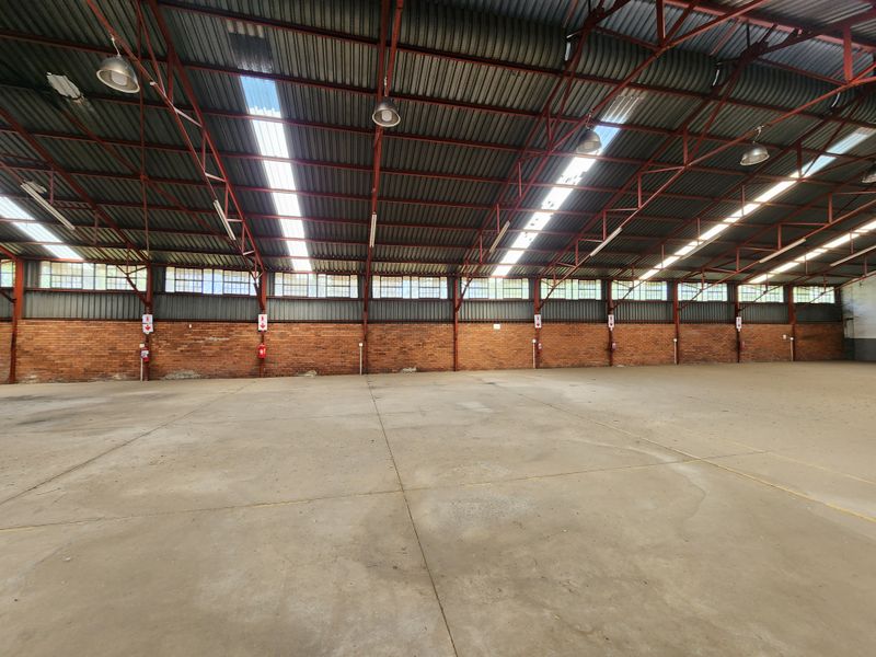 Spacious industrial warehouse featuring high exposed steel truss ceilings, abundant natural light from skylights, durable concrete flooring, and classic exposed brick walls.