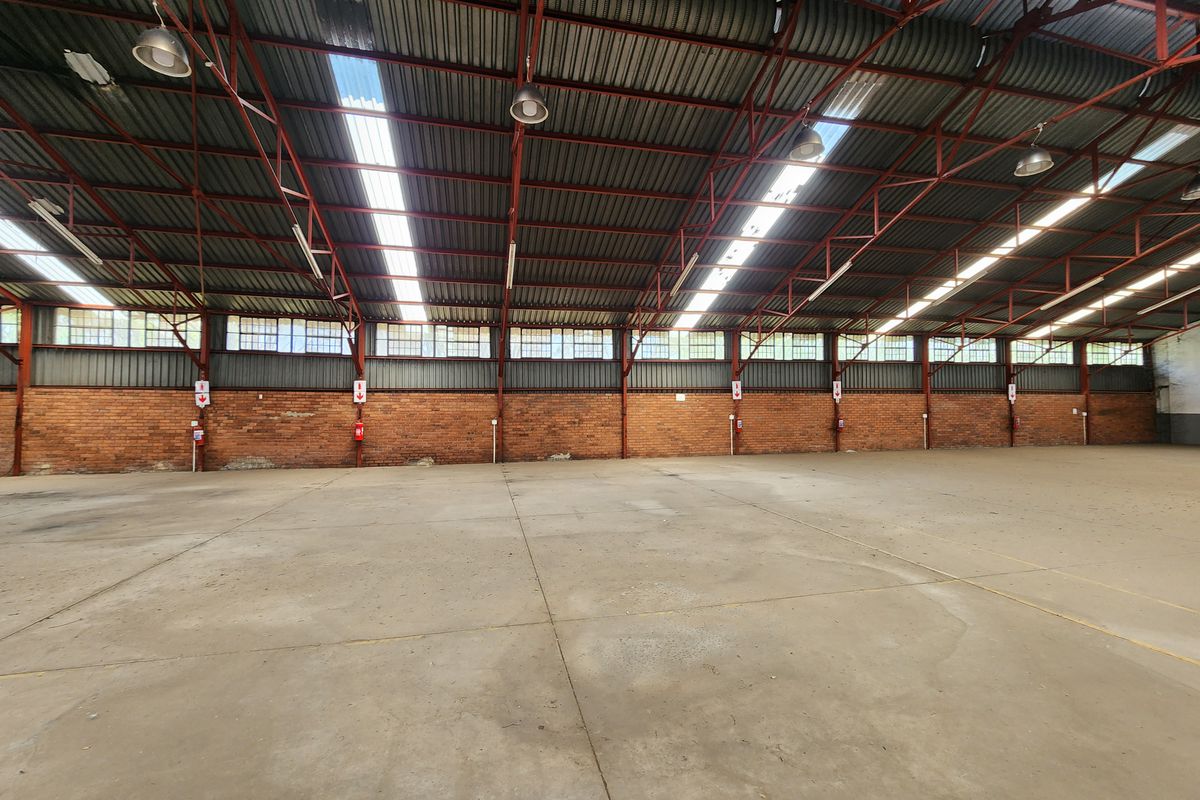 Spacious industrial warehouse featuring high exposed steel truss ceilings, abundant natural light from skylights, durable concrete flooring, and classic exposed brick walls.