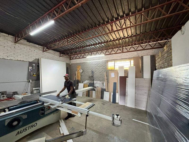Industrial workshop space featuring exposed brick walls, high-clearance metal roof structure, and integrated lighting, suitable for manufacturing or storage operations.