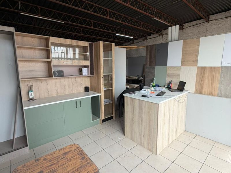 Industrial workspace featuring built-in cabinetry, a central service counter, and exposed roof trusses, suitable for a showroom or workshop environment.