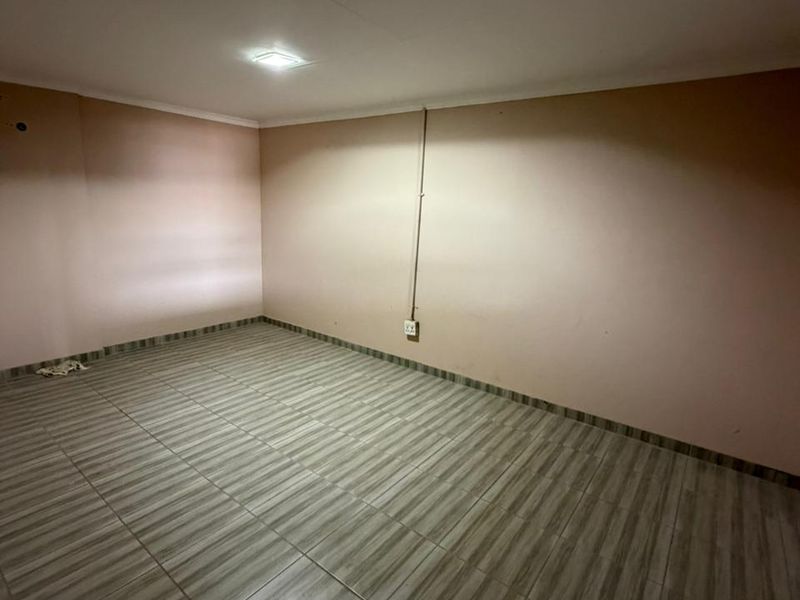 An empty, versatile industrial room featuring tiled flooring, neutral wall finishes, and a central ceiling light fixture.