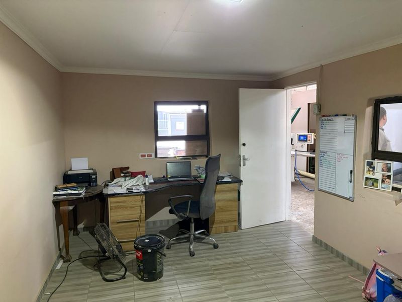 A functional office space featuring tiled flooring, a built-in desk area, and direct access to the industrial workshop floor.