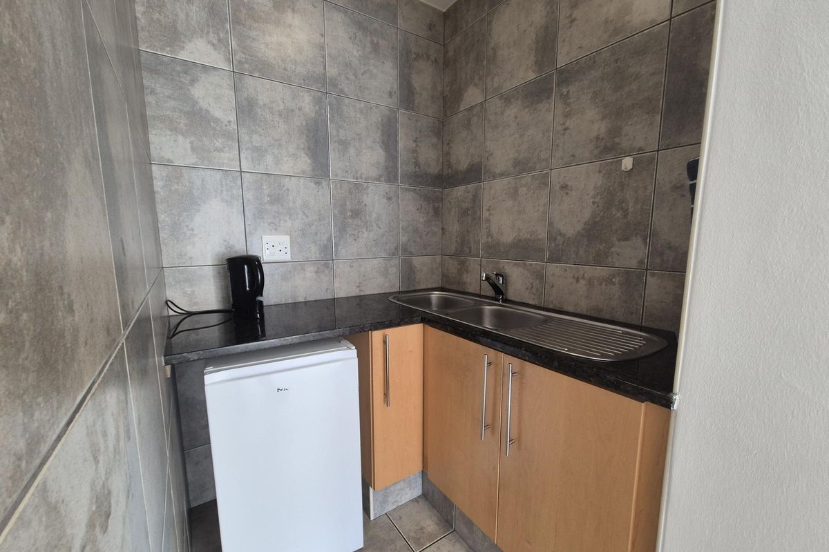 A compact kitchenette area featuring built-in wooden cabinetry, a dark stone-look countertop, and a stainless steel sink with tiled splashback.
