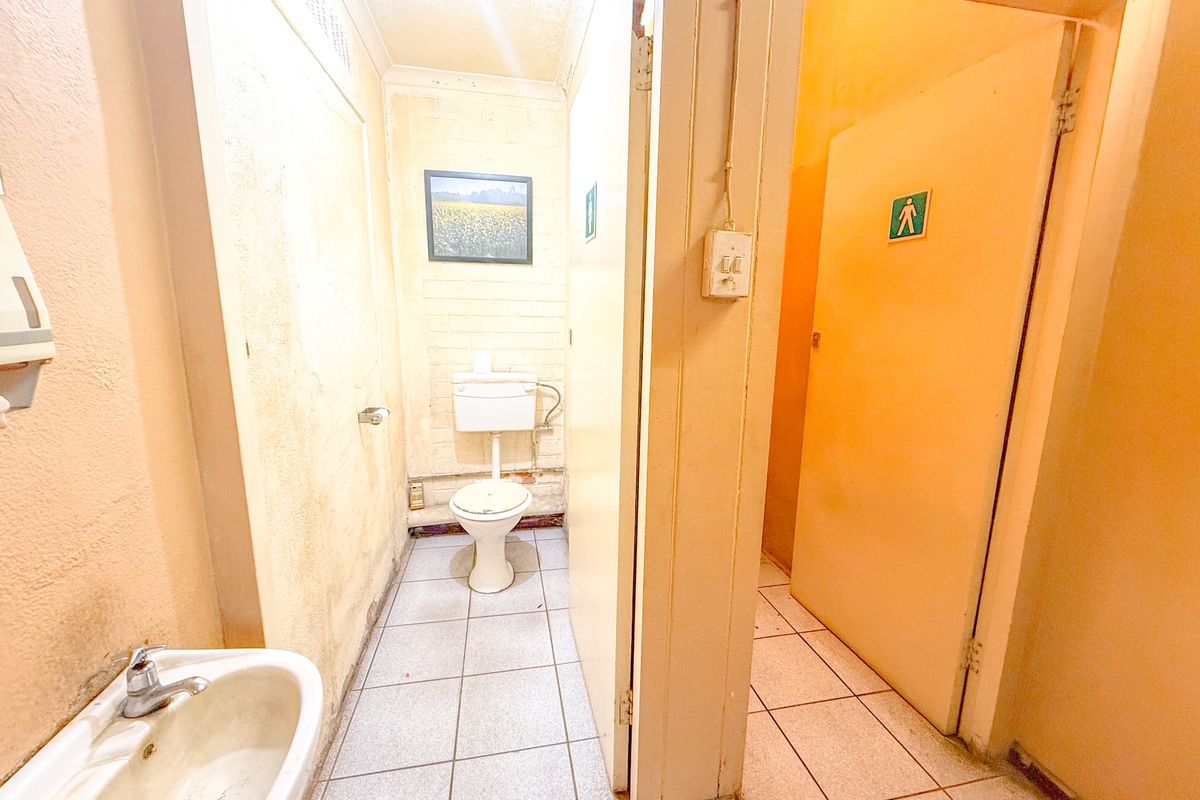 A functional industrial restroom facility featuring a ceramic basin and a separate toilet cubicle with tiled flooring and basic utility finishes.