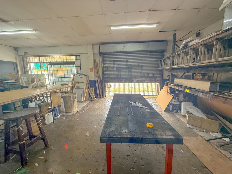 Industrial workshop space featuring a large roller shutter door, heavy-duty metal shelving, and fluorescent lighting, suitable for manufacturing or storage operations.