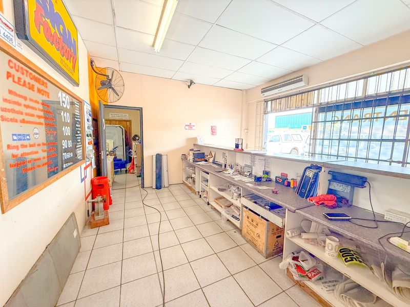 Industrial service counter area featuring tiled flooring, built-in service desk, wall-mounted fan, and security window grilles.