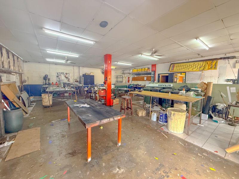 Industrial workshop space featuring open floor plan, fluorescent lighting, and structural support columns, suitable for manufacturing or storage operations.