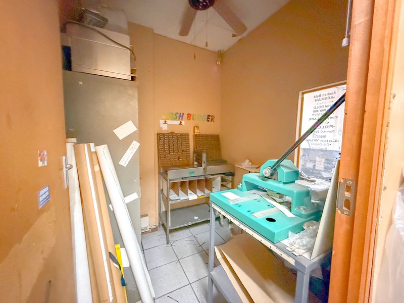 A small utility or storage room featuring tiled flooring and a ceiling fan, currently utilized for industrial printing or workshop equipment.
