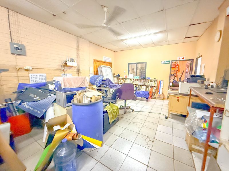 Industrial utility space featuring tiled flooring, exposed brick walls, and a suspended ceiling, suitable for storage or workshop operations.