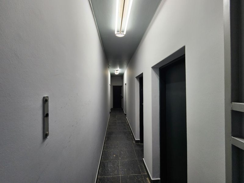A functional industrial hallway featuring tiled flooring, multiple internal access doors, and overhead fluorescent strip lighting.