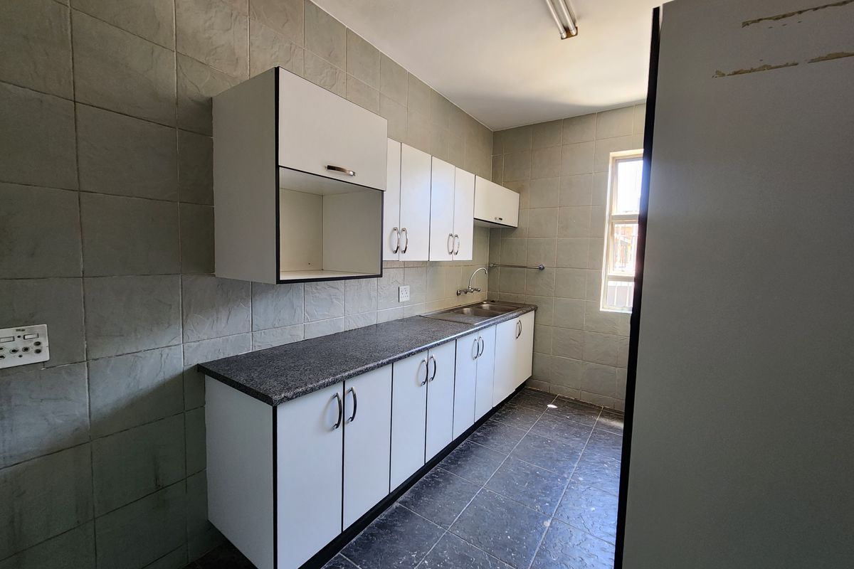 A functional industrial-style kitchen featuring built-in cabinetry, laminate countertops, a stainless steel sink, and full-height wall tiling.