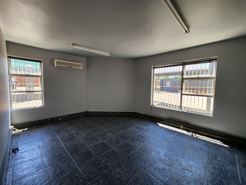 An empty office space featuring tiled flooring, air conditioning, and large windows with security bars, suitable for a professional workspace.