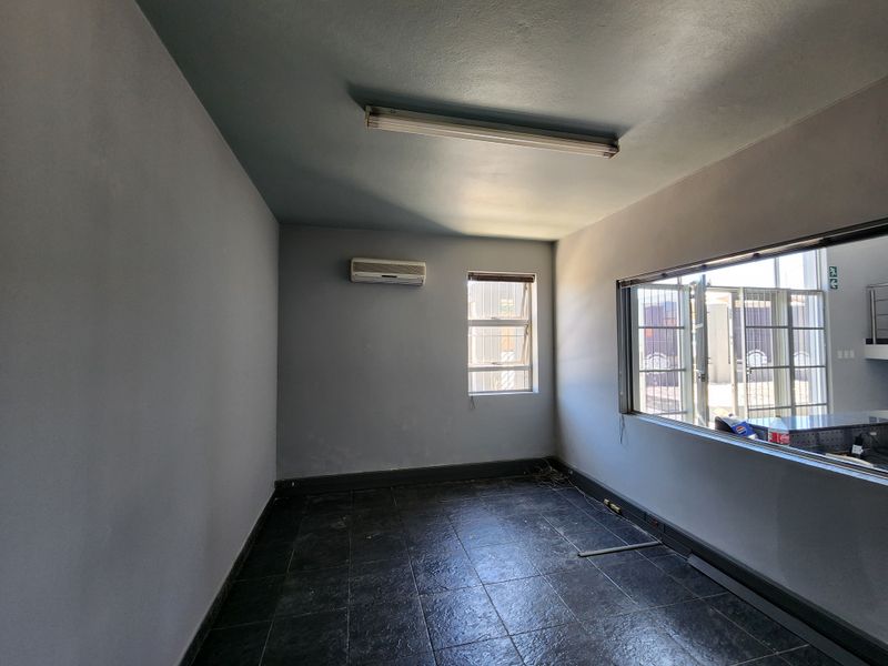 A vacant office space featuring tiled flooring, a split-system air conditioner, and a large interior window with security bars.