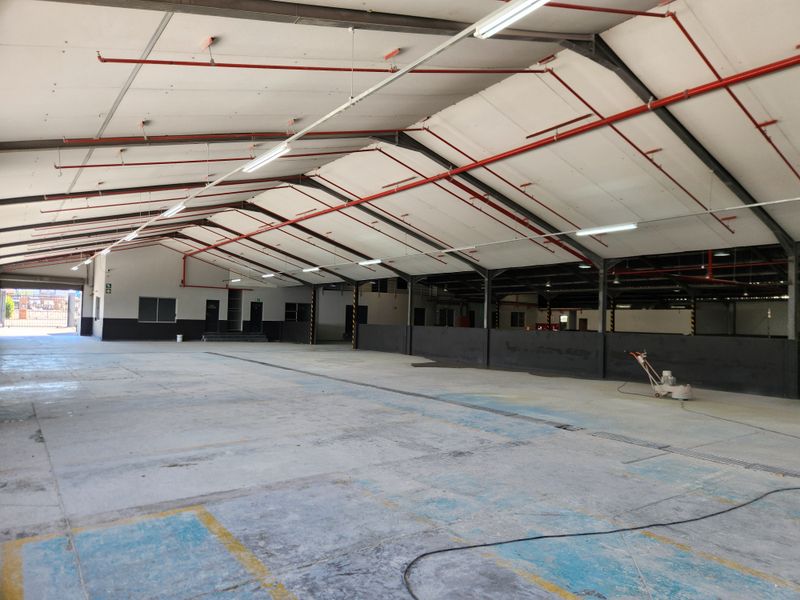 Spacious industrial warehouse featuring high ceilings with exposed steel trusses, fire sprinkler system, and durable concrete flooring, suitable for various commercial or storage operations.